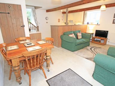 A living room and dining area with wooden table and chairs green sofas television and kitchen at Y Stabl The Old Stable in Llanbedr