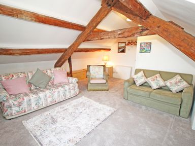 A living room with two sofas and an armchair under exposed wooden beams at Y Stabl The Old Stable in Llanbedr