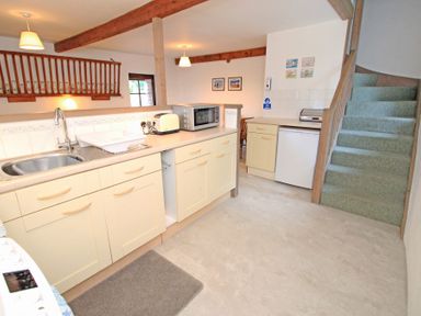 A kitchen with cream cabinets a microwave a toaster a sink and stairs with green carpet at Y Stabl The Old Stable in Llanbedr