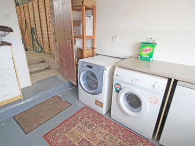 A laundry room with a washing machine, dryer, shelving unit, and a box of detergent on the counter at Y Stabl The Old Stable in Llanbedr