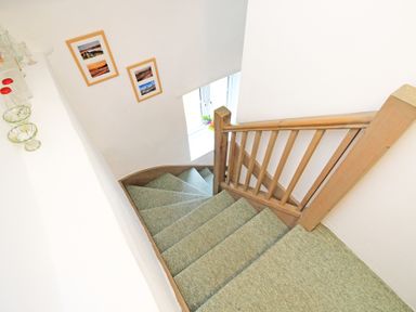 A carpeted staircase with wooden railing and framed pictures on the wall at Y Stabl The Old Stable in Llanbedr