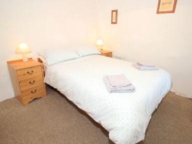 A bedroom with a double bed bedside tables with lamps and folded towels at Y Stabl The Old Stable in Llanbedr