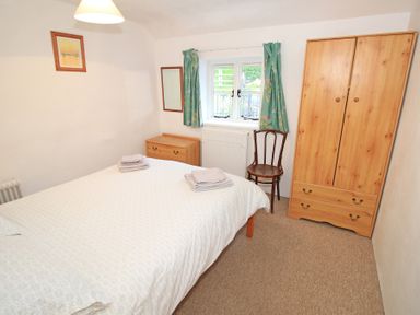 A bedroom with a bed, wooden wardrobe, chest of drawers, chair, window with green curtains and a framed picture at Y Stabl The Old Stable in Llanbedr