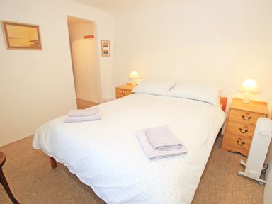 A bedroom with a double bed two bedside tables with lamps folded towels on the bed and a heater at Y Stabl The Old Stable in Llanbedr
