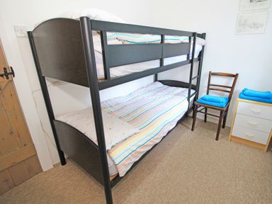 A bedroom with a black metal bunk bed striped bedding a wooden chair with blue towels and a small dresser at Y Stabl The Old Stable in Llanbedr