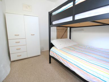 A small bedroom with a bunk bed and a white wardrobe at Y Stabl The Old Stable in Llanbedr