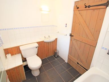 A bathroom with a toilet sink wooden door and tiled floor at Y Stabl in Llanbedr