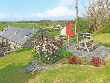 A stone building with skylights near a garden area with a wooden picnic table and flowering shrubs at Y Stabl The Old Stable in Llanbedr