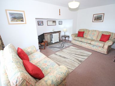 A living room with two floral sofas with red cushions a small TV on a wooden stand a radiator by a fireplace and artwork on the walls at The Farmhouse in Llanbedr