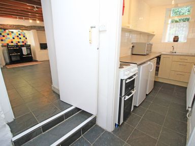 A kitchen with stove microwave and fridge adjacent to a room with a cooler and multicolored tiled wall at The Farmhouse in Llanbedr