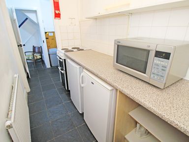 A narrow kitchen with a microwave oven refrigerator stove and tiled floor at The Farmhouse in Llanbedr