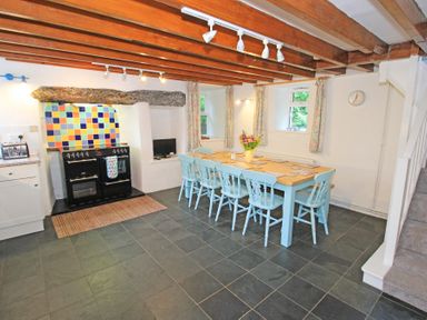 A kitchen with a wooden table and six chairs near a black stove with colorful tiled wall at The Farmhouse in Llanbedr