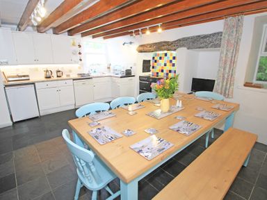 A kitchen dining area with a wooden table and blue chairs and a tiled backsplash at The Farmhouse in Llanbedr
