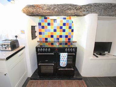 A kitchen area with a black stove under a stone beam and colorful tiled wall at The Farmhouse in Llanbedr