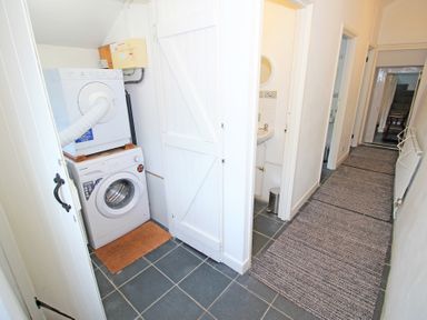 A hallway with a tiled floor and rugs showing a laundry area with stacked washing machine and dryer and a small sink at The Farmhouse in Llanbedr