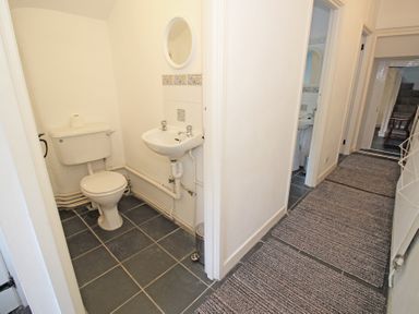 A hallway with grey floor mats leading to a small bathroom with a toilet and sink at The Farmhouse in Llanbedr