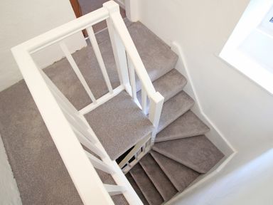 A carpeted staircase with white railings and gray carpet at The Farmhouse in Llanbedr