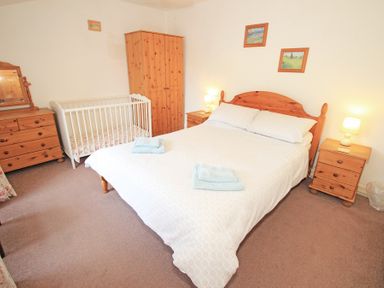 A bedroom with a double bed two bedside tables with lamps a wardrobe a chest of drawers and a baby cot at The Farmhouse in Llanbedr