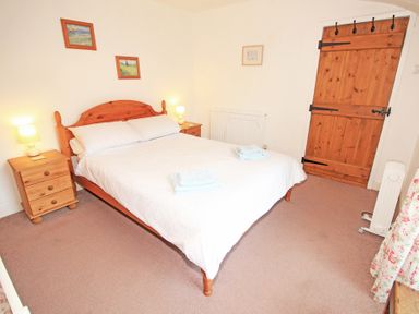 A bedroom with a wooden double bed white bedding bedside tables lamps wooden door and carpet at The Farmhouse in Llanbedr