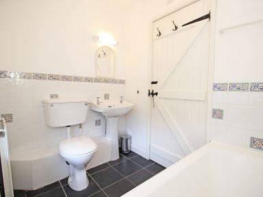 A bathroom with a toilet sink and bathtub with tiled walls and a wooden door at The Farmhouse in Llanbedr