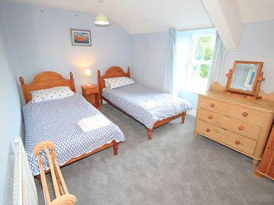 A bedroom with two single beds bedside table with lamp window with curtains and a wooden dresser with mirror at The Farmhouse in Llanbedr