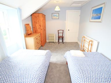 A bedroom with two single beds a wooden wardrobe a chest of drawers a chair and a radiator at The Farmhouse in Llanbedr