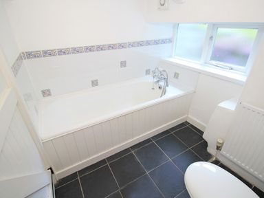 A bathroom with a white bathtub tiled walls and a window at The Farmhouse in Llanbedr