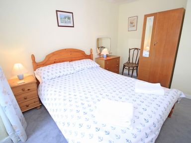 A bedroom with a double bed with anchor patterned bedding a wooden wardrobe a dressing table with a lamp a wooden chair and two framed pictures on the wall at The Farmhouse in Llanbedr