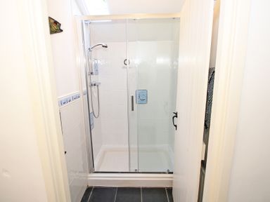 A shower with glass sliding doors and a handheld showerhead in a tiled bathroom at The Farmhouse in Llanbedr