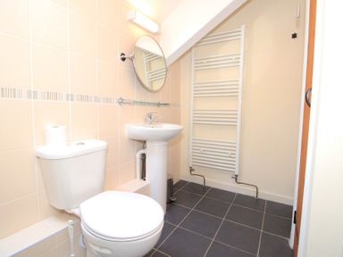 A bathroom with a toilet sink round mirror and towel radiator at The Farmhouse in Llanbedr