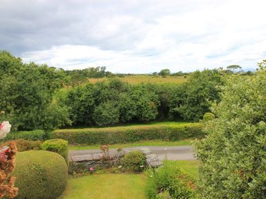 A garden with trimmed hedges and bushes overlooking fields and trees at The Farmhouse in Llanbedr