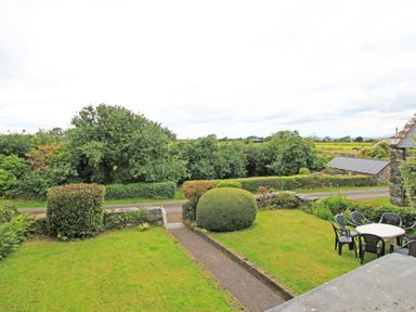 A garden with trimmed bushes and a patio table with chairs at The Farmhouse in Llanbedr