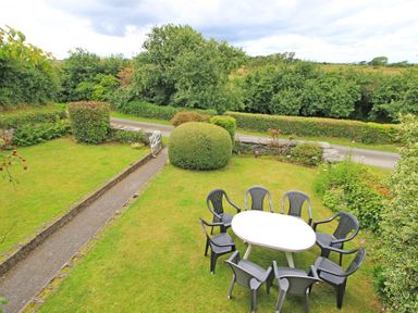 A garden with a white table and eight black chairs a pathway and trimmed bushes at The Farmhouse in Llanbedr