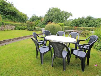 A garden with a white table and black chairs on the grass at The Farmhouse in Llanbedr