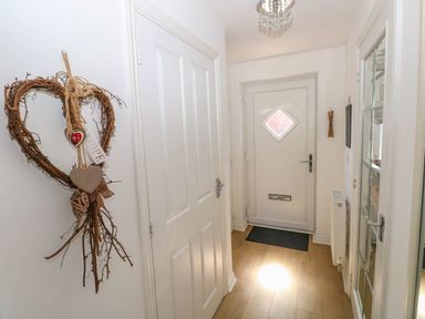 A hallway with a white front door a wooden floor a decorative heart hanging on the wall and a glass-paneled door at Ty Bach Twt Llanelli