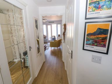 A hallway with wooden floor leading to a living room with chairs and glass doors at Ty Bach Twt Llanelli