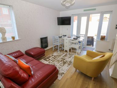A living room with a red leather sofa an ottoman a yellow armchair a white dining table with chairs and a wall-mounted television at Ty Bach Twt Llanelli