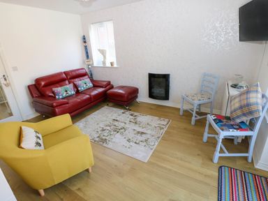 A living room with a red sofa and matching ottoman a yellow armchair two blue chairs a wall-mounted TV and a small white cabinet at Ty Bach Twt Llanelli