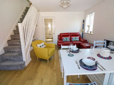 A living area with a white dining table set with plates and glasses a yellow armchair a red leather sofa stairs with grey carpet and a window at Ty Bach Twt Llanelli