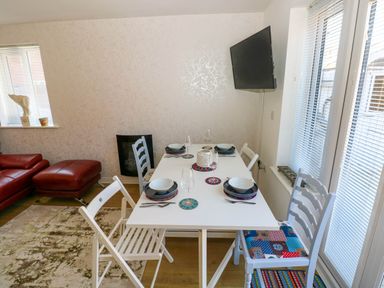 A dining area with a white table set for four with mismatched chairs near a window and red sofa at Ty Bach Twt Llanelli