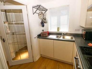 A kitchen with a sink under a window a glass panel door and pots hanging on a rack at Ty Bach Twt Llanelli