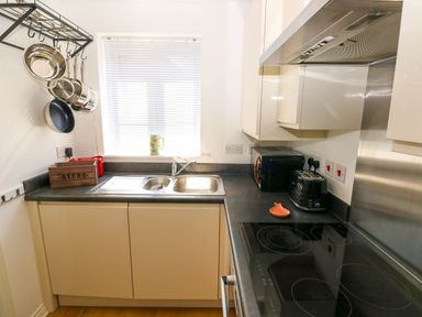 A kitchen with a sink under a window and hanging pots and pans at Ty Bach Twt Llanelli