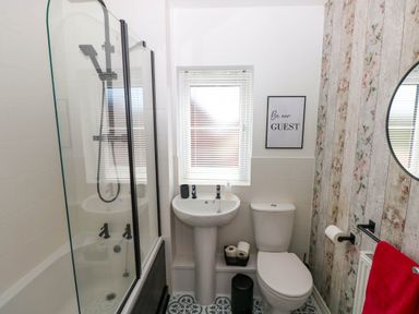 A bathroom with a bathtub and shower, a pedestal sink, a toilet, and a floral patterned wall at Ty Bach Twt Llanelli