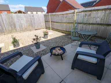 A small outdoor patio with two cushioned chairs fire pit three potted plants and a metal table with two chairs at Ty Bach Twt Llanelli