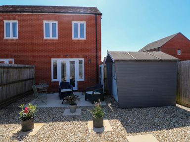 A backyard with patio furniture and potted plants next to a shed at Ty Bach Twt Llanelli