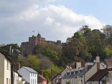 A castle on a hill above houses and trees at Little Dragons in Dunster near Minehead