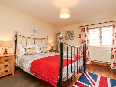 A bedroom with a metal bed frame red blanket bedside tables with lamps and a window with floral curtains at Little Dragons Dunster near Minehead