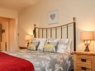 A bedroom with a metal bed frame bedside tables with lamps and pillows that say happy at Little Dragons in Dunster near Minehead