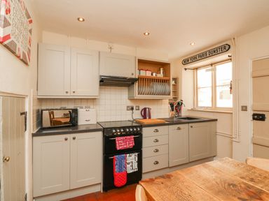 A kitchen with grey cabinets a black stove and a wooden table at Little Dragons in Dunster near Minehead