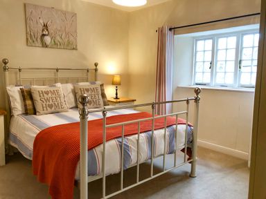A bedroom with a metal bed frame pillows with home sweet home text bedside tables a lamp and a window with curtains at Little Dragons Dunster near Minehead